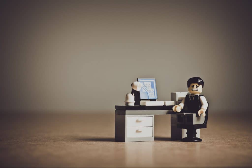 Een wanhopig kijkend figuurtje van LEGO achter een bureau met een computer, wellicht wil hij zijn studieschuld aflossen en kan hij wel wat lessen gebruiken