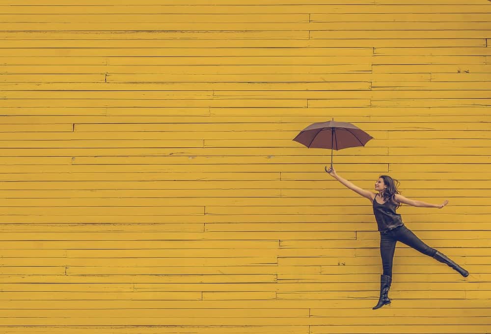 Een vrouw zweeft vrolijk aan een parapluutje door de lucht, symbolisch voor wat je gaat doen als je studieschuld is afgelost.