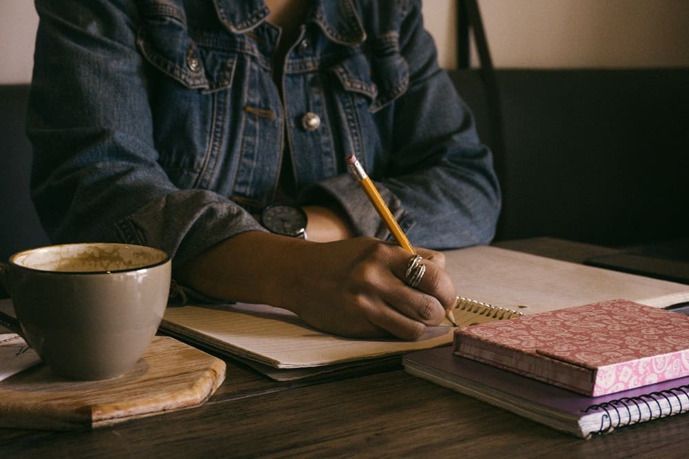 Een vrouw schrijft met een potlood in een kladblok, het is goed om te checken of je je studieschuld mag aftrekken van de belasting.