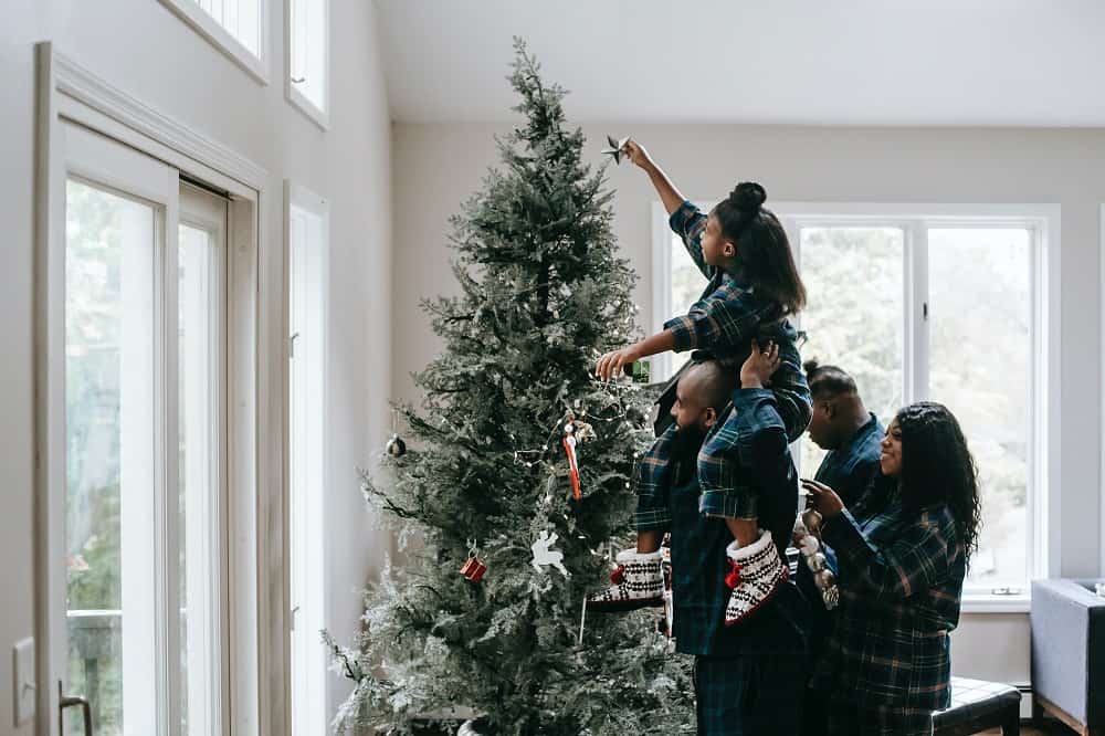 Gezinsleden versieren een kerstboom met zelfgemaakte sterren en versiersels, een handige tip voor goedkope kerstversiering