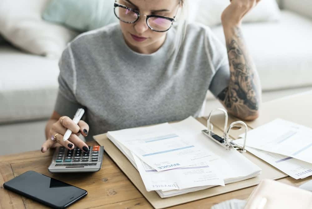 Een vrouw met een bril en tatoeages met een rekenmachine, ze is wellicht aan het berekenen hoe ze haar studieschuld versneld kan aflossen