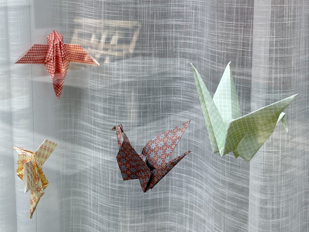 Een raam met vitrage en kleurrijke kraanvogels (origami)