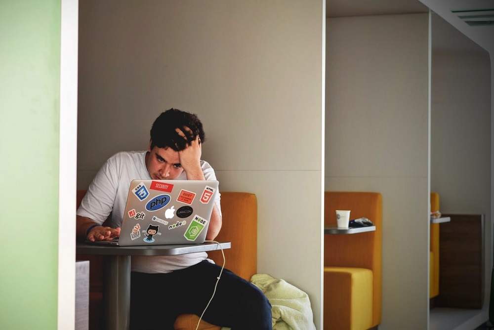 Een jonge man kijkt moedeloos naar z'n laptop, z'n hand zit in z'n haar (hij heeft zeker geen zin om meteen iets te doen, gok ik zo)