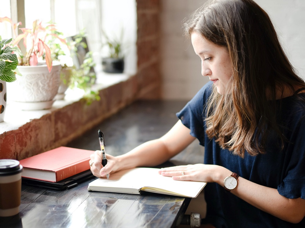 Een jonge vrouw schrijft in een notitieboek, wellicht maakt ze een plan om volgende maand te gaan sparen