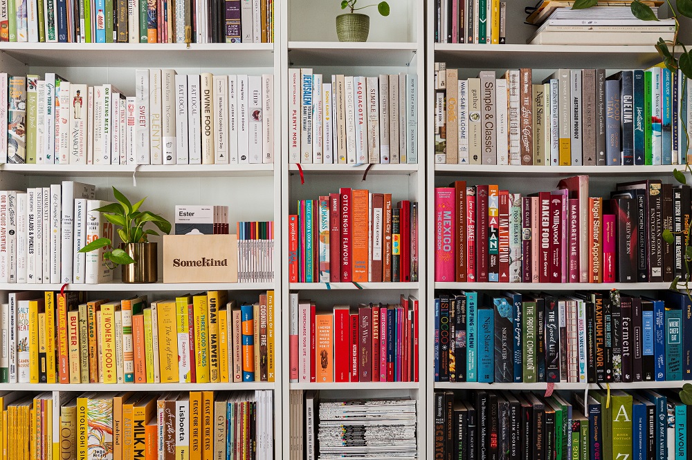 Een grote witte boekenkast helemaal vol met op kleur gesorteerde boeken