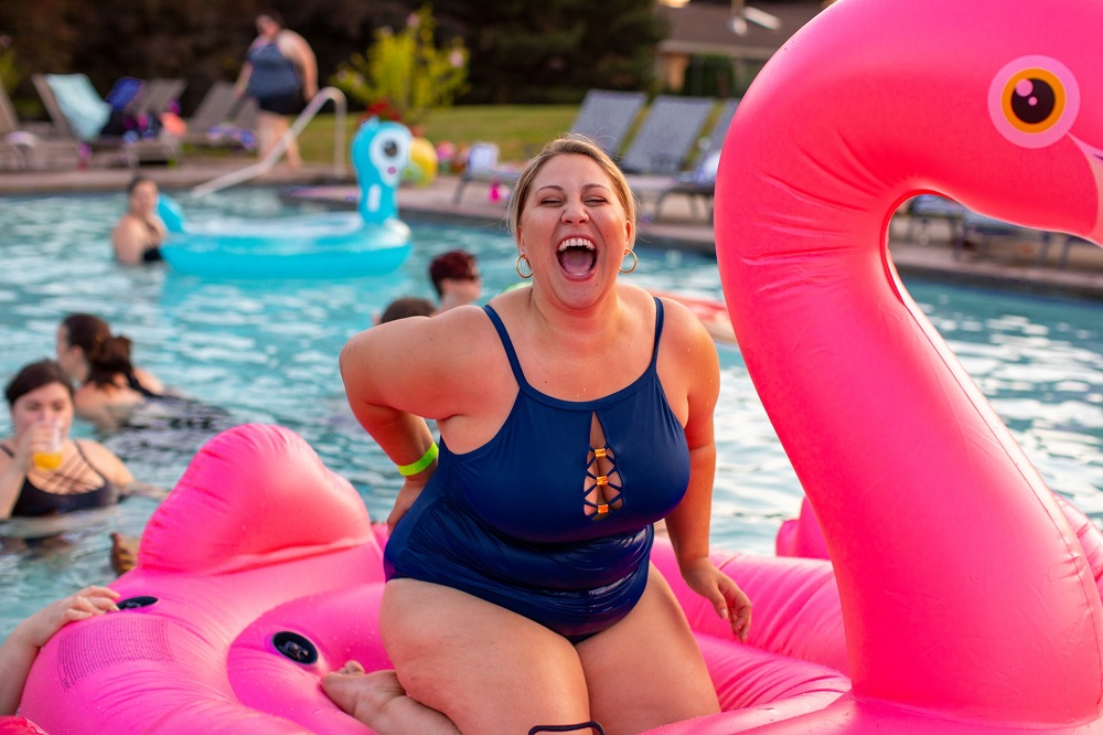Een lachende vrouw zit op een roze opblaasflamingo in een zwembad (zou ze de tips van DUO voor de zomer al hebben gecheckt?)