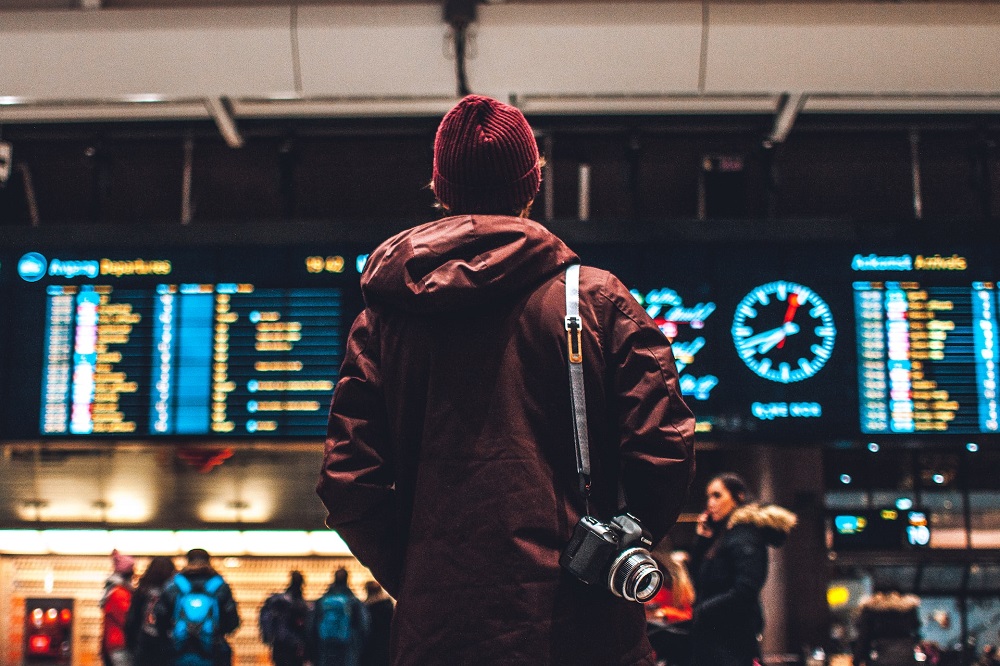 Een jongeman staart op een vliegveld naar een digitaal bord met vertrektijden (hij neemt wellicht een tussenjaar omdat de basisbeurs pas terugkeert in 2023)