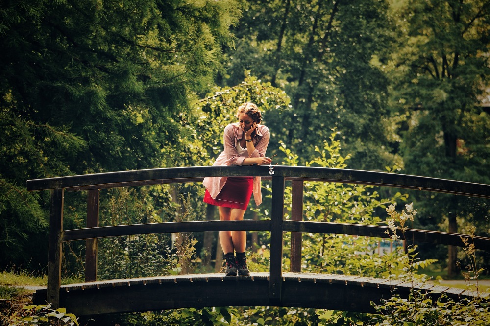 Een vrouw staat in het bos op een bruggetje en kijkt mijmerend omlaag (het is bijna oud en nieuw 2023, wellicht is ze aan het terugblikken)